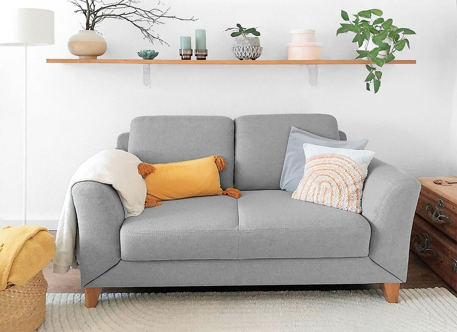 Skandi-Boho-Vintage Wohnzimmer mit grauem Sofa, hellem Holz, orangefarbenem Akzentkissen und hellen Wänden.