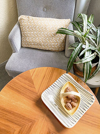 Gemütliche Sitzecke mit Holz-Couchtisch, grauem Sessel, Topfpflanze und Tischschale in Vintage-Design mit grau-gelben Akzenten.